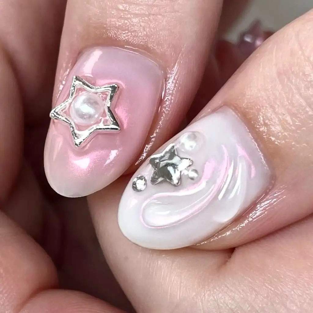 Two nails in pearl pink and white with a silver star charm and a pearl