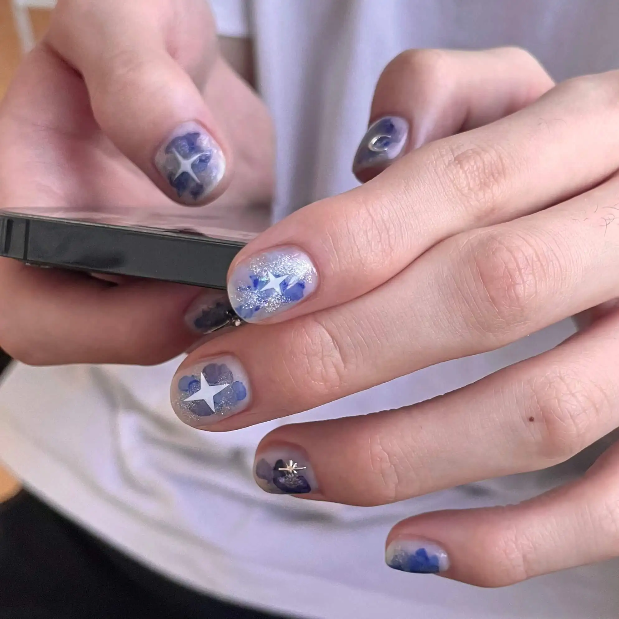 Short nails with blue airbrushed crosses and stars on a milky base